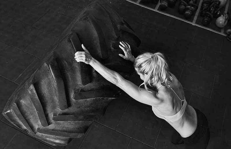 Vista cenital de una mujer realizando entrenamiento funcional al empujar un neumático grande en el mejor gimnasio de Caballito.